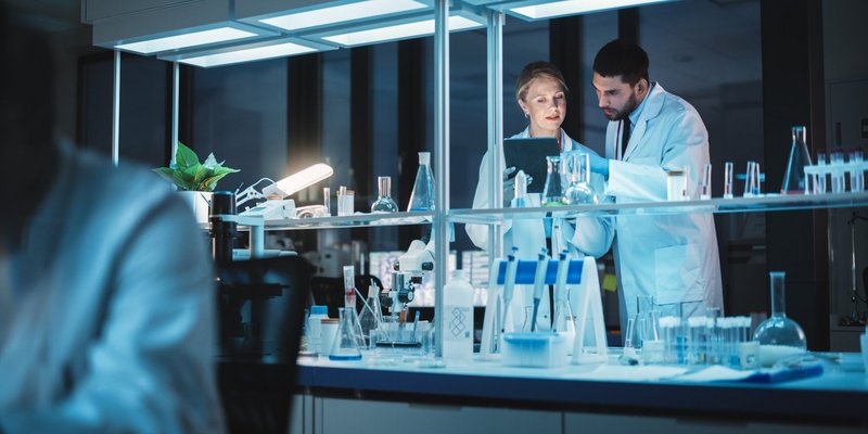 Female and Male Medical Research Scientists Have a Conversation While Conducting Experiments in a Petri Dish, Writing Analysis Results on a Tablet Computer. Modern Biological Science Laboratory.